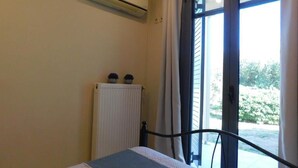 A bedroom with a bed, an air conditioning unit, a radiator, and a window with curtains.