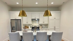 A modern kitchen with white cabinets, a stainless steel refrigerator, a double oven, and a marble countertop. There are four bar stools with wooden legs and grey fabric seats. Two gold pendant lights hang above the island. - 2-bedroom villa in tranquil Provo with refreshing AC (Provo)