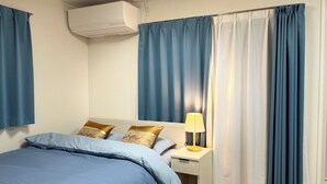 A hotel room with a bed, nightstand, lamp, curtains, and an air conditioning unit.