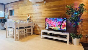 A dining area with a wooden wall, a TV on a stand, and a potted plant.