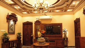 A luxurious room with a marble floor, a large chandelier, a statue, and a flat-screen TV. - SK Grand Palace (Puducherry)
