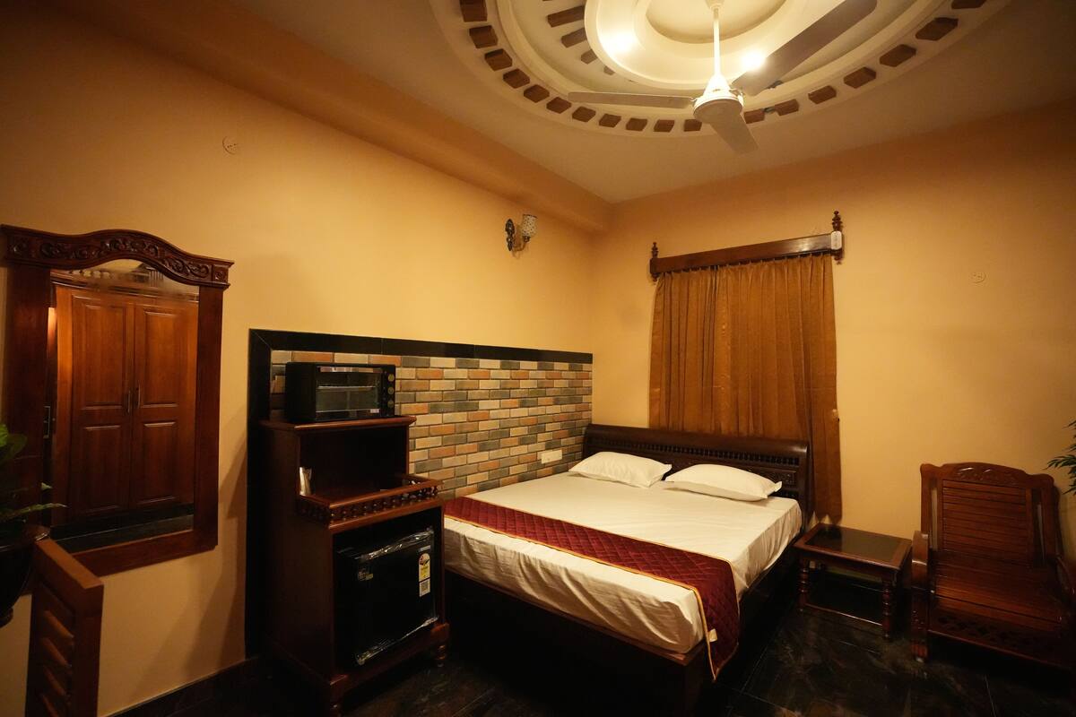 A hotel room with a brick-patterned headboard, a wooden wardrobe, a bedside table, and a ceiling fan.