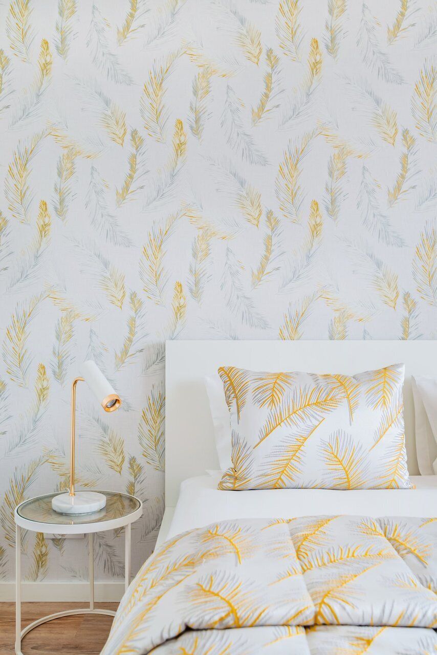 A bedroom with a bed, a bedside table with a lamp, and a wall with a leaf pattern.