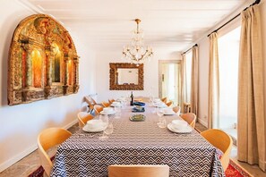 Ein Esszimmer mit langem Tisch, gedecktem für eine Mahlzeit, aufwändigen Wandverzierungen und einem Kronleuchter.