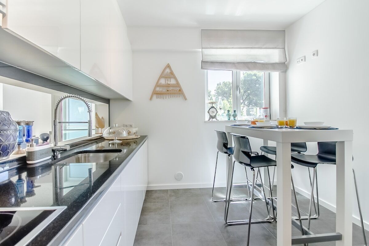 Une cuisine moderne avec un plan de travail noir, des meubles blancs et un coin repas comprenant une table blanche et des chaises noires.