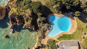 Luftaufnahme eines Küsteneigentums mit Schwimmbad, Felsenküste und üppiger Vegetation.
