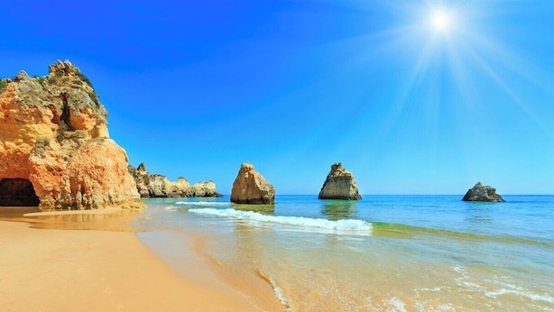 Ein Strand mit klarem, blauem Wasser, einem Sandstrand und Felsformationen.