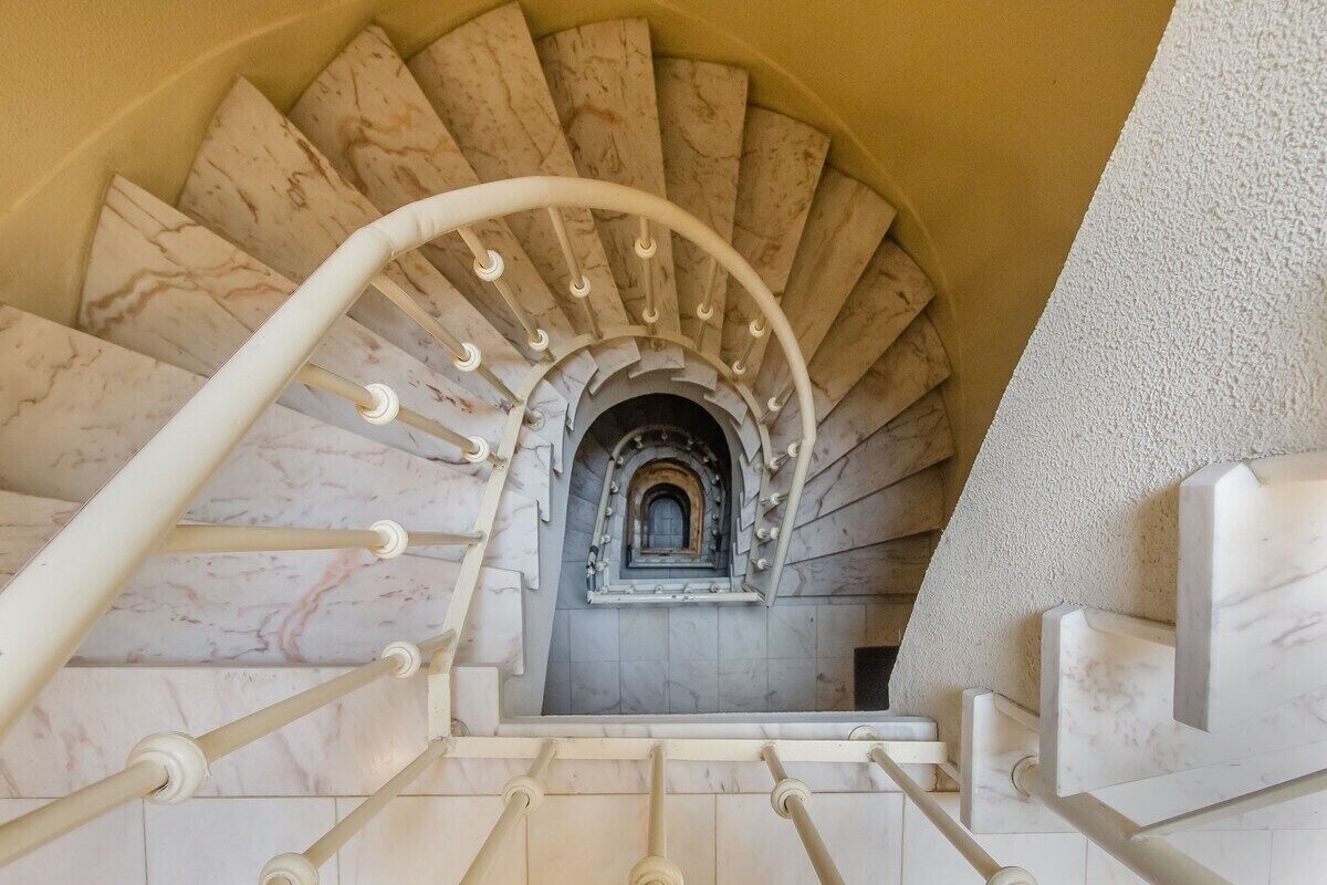 A marble staircase with a white handrail and a central archway.