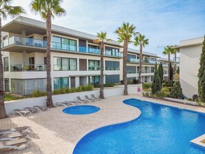 Ein modernes Hotel mit Schwimmbad, Palmen und Liegestühlen.