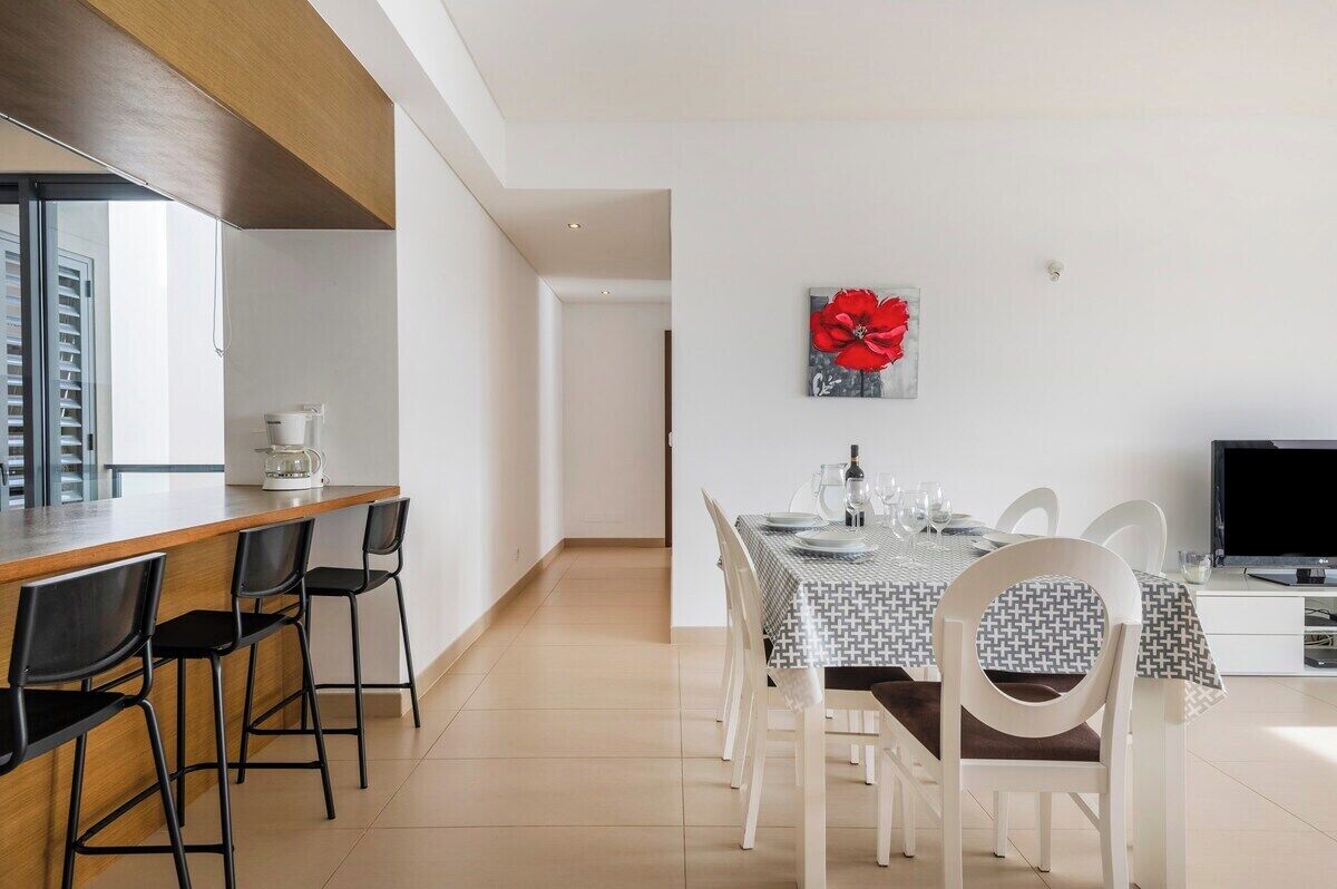 A dining area with a table set for four, a coffee machine, and a TV on a stand.