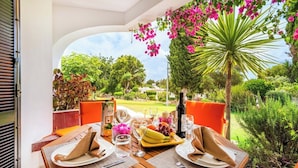 Ein Essbereich im Freien mit einem Tisch für zwei Personen, umgeben von üppiger Bepflanzung und Blick auf einen gepflegten Garten.