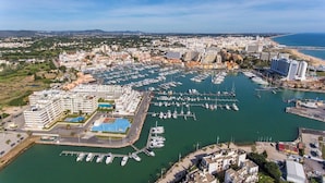 Vista aérea de un puerto deportivo con numerosas embarcaciones amarradas, un gran complejo hotelero con varias construcciones, y una costa al fondo.