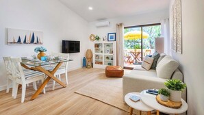 Un moderno salón con una mesa de vidrio, sofás blancos y vistas al exterior.