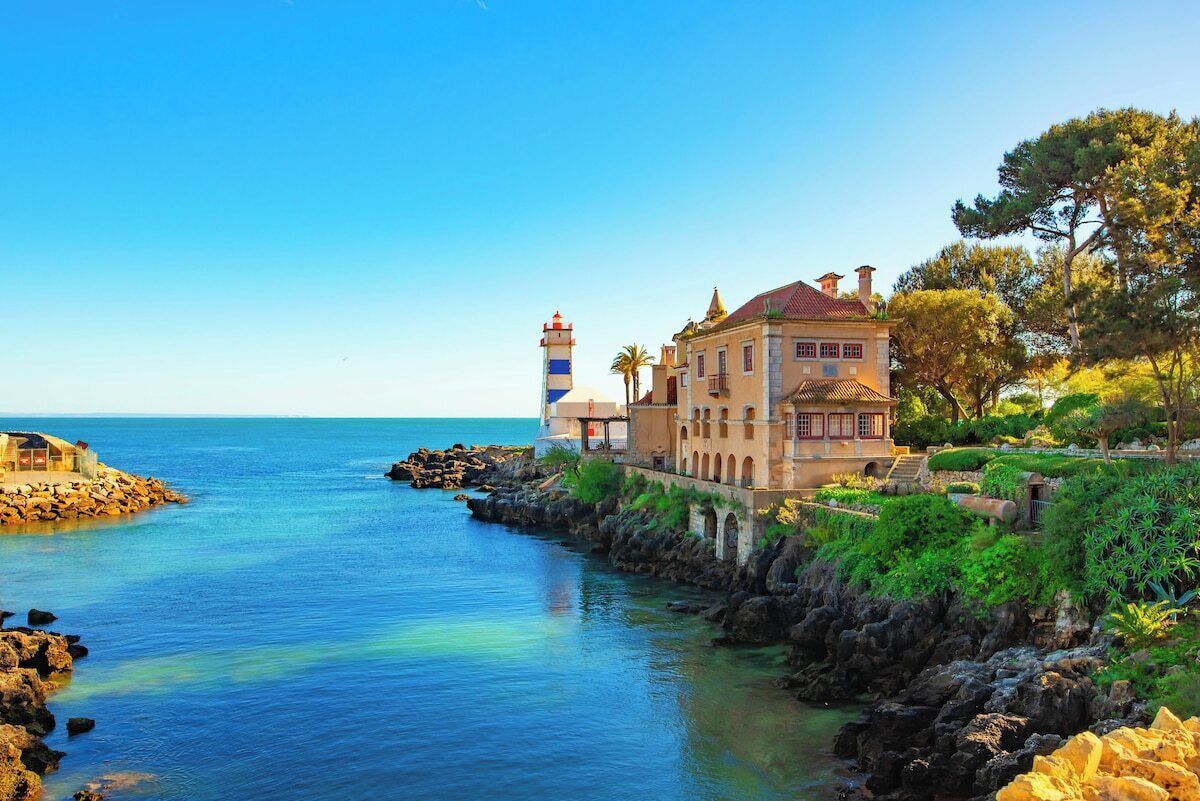 Un edificio costero con un faro, costa rocosa y mar azul cristalino.