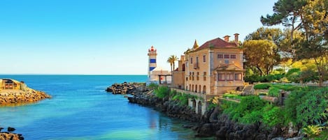 A coastal building with a lighthouse, rocky shoreline, and clear blue sea.