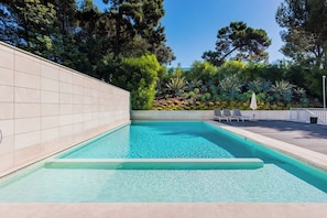 Ein Swimmingpool mit gefliesten Wänden, umgeben von Grünpflanzen und Bäumen.