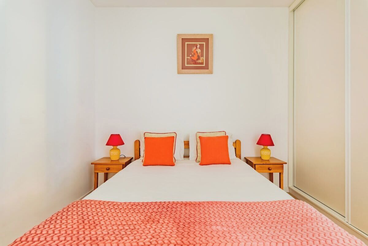 A bedroom with a bed, two pillows, two bedside tables with lamps, a framed picture on the wall, and a patterned blanket.