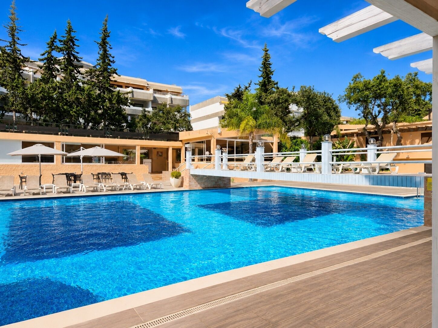 Ein Pool mit Liegestühlen und Sonnenschirmen, umgeben von Bäumen und Gebäuden.