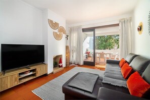 A modern living room with a flat-screen TV, a sofa, a fireplace, and a sliding glass door leading to an outdoor area. - Balaia Sunshine Apartment (Olhos de Água)