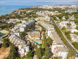 An aerial view of a coastal residential area with modern buildings, a swimming pool, and a road. - Balaia Sunshine Apartment (Olhos de Água)