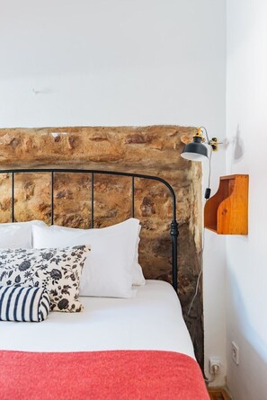 Ein Bett mit steinverkleidetem Kopfteil, einer Nachttischlampe und einem Holzbodenregal.