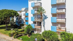 Un edificio residencial de varios pisos con balcones, cielo despejado y un jardín bien cuidado.