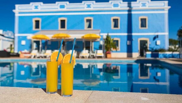 Une piscine avec deux verres d’une boisson orange et un bâtiment bleu en arrière-plan.