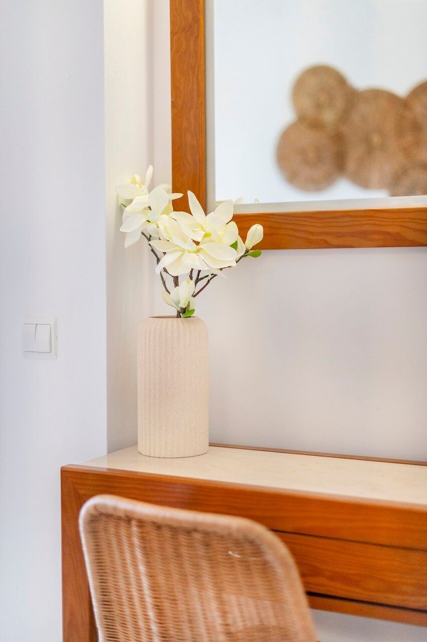 A corner desk with a vase of white flowers, a wicker chair, and a framed artwork on the wall.