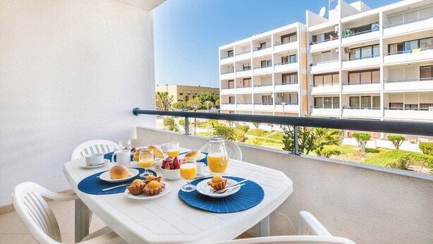 Ein Balkon mit einem Tisch, gedeckt für das Frühstück, inklusive Tellern, einer Karaffe und einer Obstschale.
