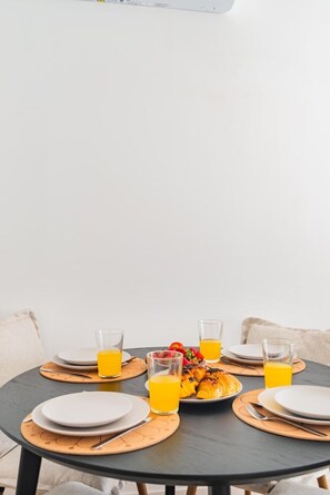 Ein runder Esstisch mit Tellern, Besteck und Gläsern Orangensaft, vor einer schlichten Wand.