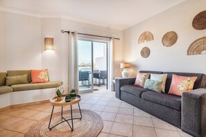 Ein Wohnzimmer mit einer Couch, einem runden Couchtisch und einem Balkon mit Gartenmöbeln.