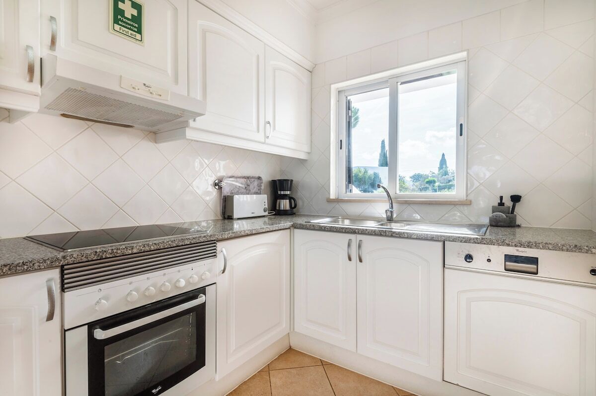 A kitchen with white cabinets, a built-in oven, a coffee maker, and a window with a view.