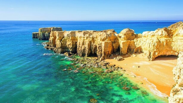 Un paisaje costero con acantilados, aguas turquesas cristalinas y una playa arenosa.