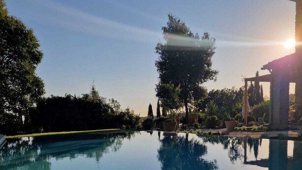 Una piscina limpida che riflette alberi e una struttura a pergola.
