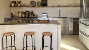 Una cucina moderna con una grande isola, sgabelli da bar, elettrodomestici in acciaio inossidabile e travi in legno al soffitto.