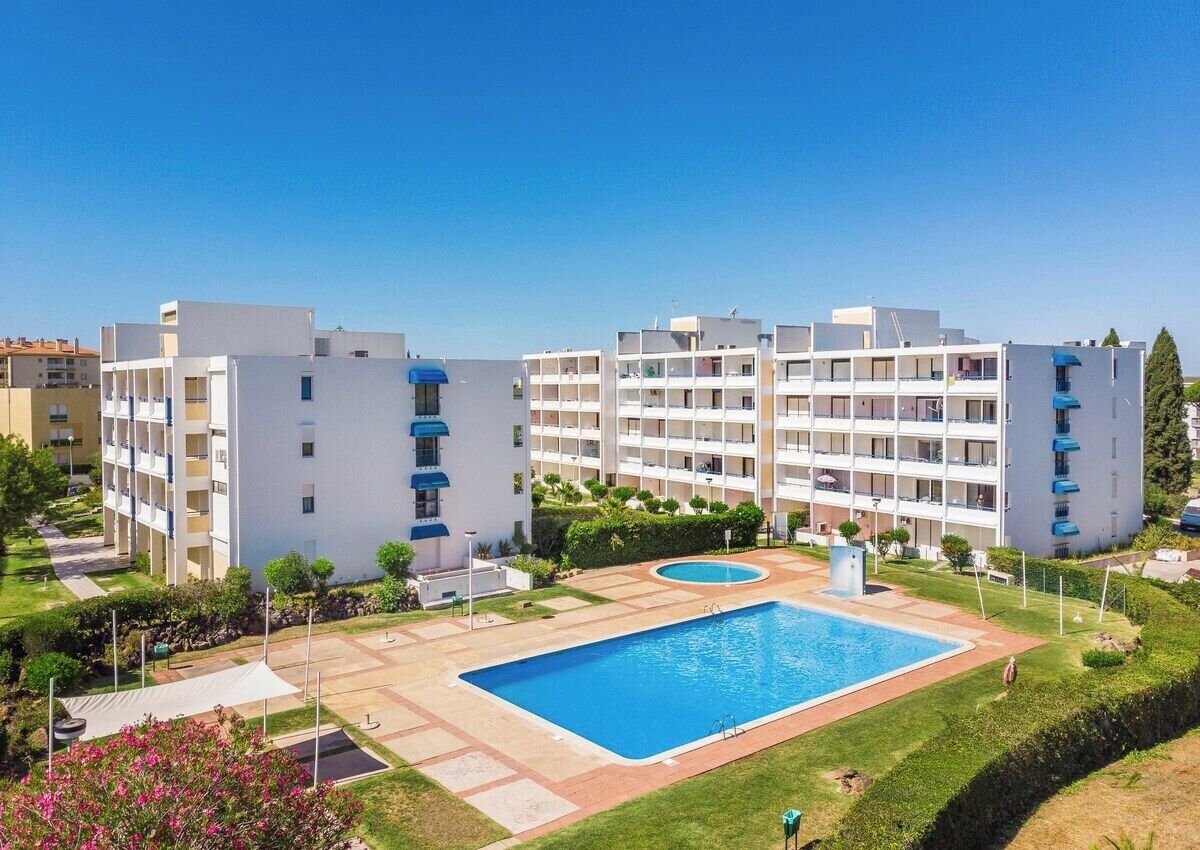 A modern hotel with multiple floors, a central swimming pool, and a well-maintained garden.