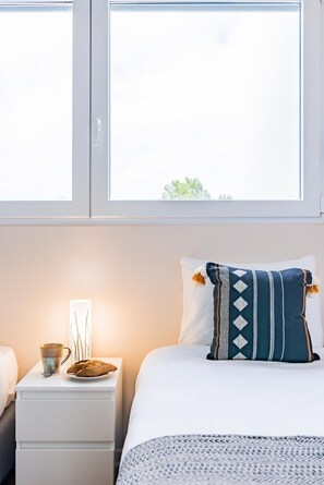 Ein Hotelzimmer mit einem Bett, einem Nachttisch mit Tasse und Speisenplatte, sowie einem Fenster mit Blick auf Grünflächen.