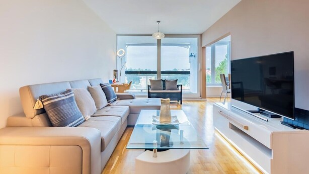 Sala de estar moderna com sofá, mesa de centro, TV e janelas amplas com vista.
