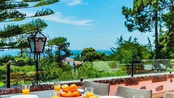 Een terras met een ontbijttafel, compleet met croissants en sinaasappelsap, onder een grote oranje parasol.