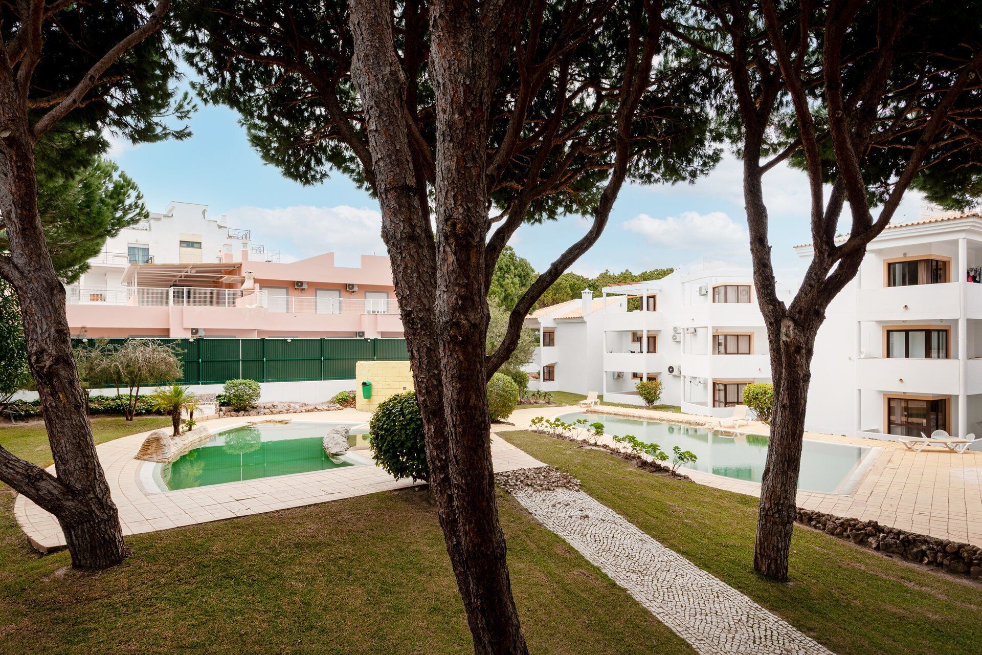 A residential area with multiple white buildings, a swimming pool, and trees.