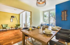Ein Essbereich mit einem Holztisch, gedeckt für vier Personen, Stühle, einer Lampe und Blick durch eine Glastür.