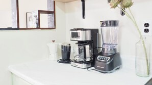 A kitchen with a coffee maker, blender, and a shelf with decorative items.