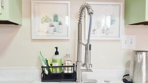 A bathroom with a modern faucet, a sink, a coffee maker, and two framed botanical illustrations on the wall.