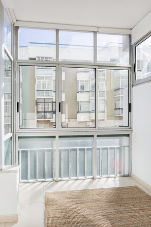 Ein Zimmer mit großen Fenstern, einem gewebten Teppich und Blick auf ein Gebäude mit Balkonen.