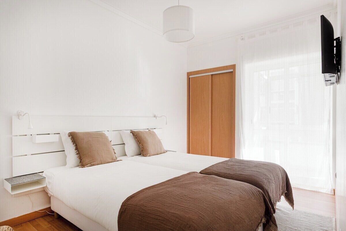 A bedroom with a bed, bedside tables, a wardrobe, a television, and a window with curtains.