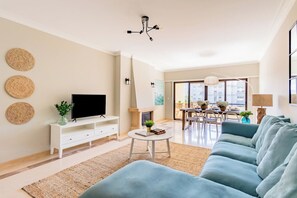 Ein modernes Wohnzimmer mit Flachbildfernseher, einer Couch, einem Essbereich mit Tisch und Stühlen sowie einem Kamin.