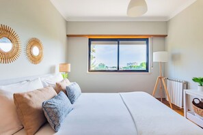 Ein modernes Schlafzimmer mit einem großen Bett, einem Fenster mit Blick auf die Stadt, einer Lampe und einer Heizung.