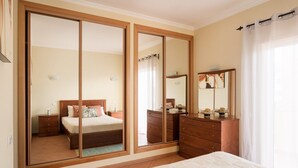 A bedroom with a sliding door closet, a bed with a white comforter, a wooden dresser, and a mirror. - Central Albufeira Stay | Balcony & AC (Albufeira)