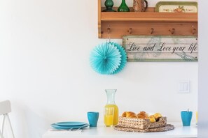 Eine Küche mit einem Holzboden, einem blauen Papierfächer, einer Glasgießkanne und einem Korb mit Croissants.