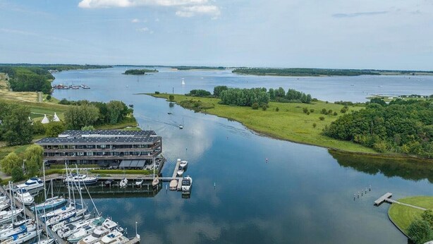 Ein Yachthafen mit vertäuten Booten, ein Gebäude mit flachem Dach und ein ruhiger Fluss.